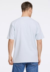 Lyhyet hihat, vaaleansininen t-paita nähtynä takaa, jossa on pyöreä kaula-aukko ja rento leikkaus. Tasainen puuvillakangas, jossa ei ole näkyviä kuvioita.