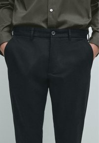 Černé kalhoty se štíhlým střihem a hladkým povrchem, s plochým předním designem, bočními kapsami a knoflíkovým zapínáním na pevném pase.