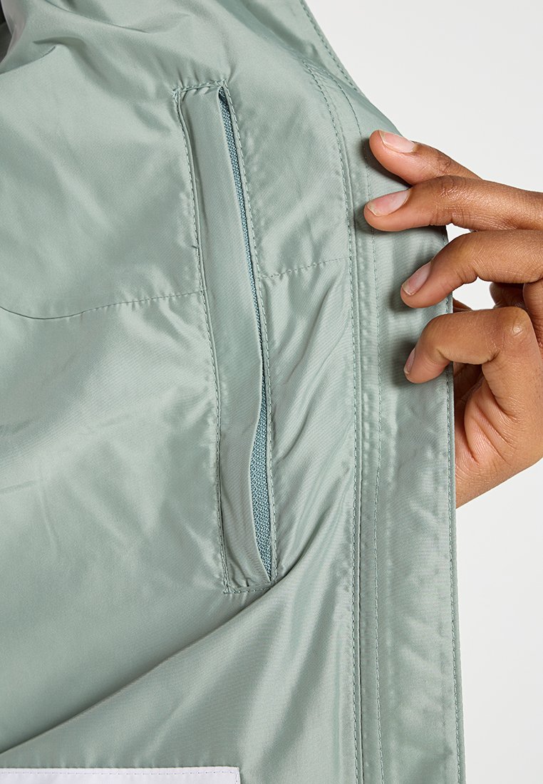 Leuchtend grüne Nylonjacke, Innenansicht mit einer Reißverschlusstasche. Hand hält den Stoff und hebt die Textur und die Nähdetails hervor.