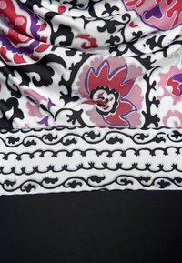 Blommönstrad tyg i nyanser av röd, lila och svart, med intrikata detaljer och ett horisontellt svart band längst ner.