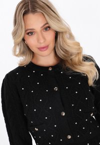 Czarny kardigan wełniany z teksturowanym wzorem, złotymi guzikami i srebrnymi ozdobami równomiernie rozmieszczonymi z przodu.