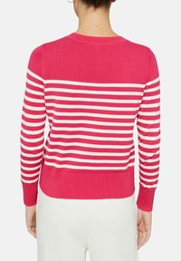 Kobieta ubrana w sweter z długim rękawem w różowo-białe poziome paski, widoczna z tyłu, w połączeniu z białymi spodniami.