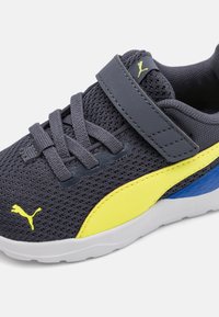 Chaussure de sport en maille grise avec des accents jaunes et bleus, dotée d'une sangle Velcro et d'un tissu texturé, conçue pour le confort et le soutien.