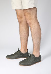 Grüne lederne Schnürschuhe mit einer hellbraunen Sohle, die dezente Nähte und ein minimalistisches Design aufweisen, die den Knöchel freilegen und eine strukturierte Oberschicht besitzen.
