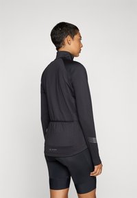 Black long-sleeve cycling jersey with a high collar, textured fabric, rear pocket, and reflective detailing on the sleeves.