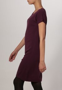 Abito a maniche corte con scollo a V in un tessuto a maglia viola scuro, dalla silhouette aderente e dettagli a coste sulle maniche, progettato per arrivare a metà coscia.