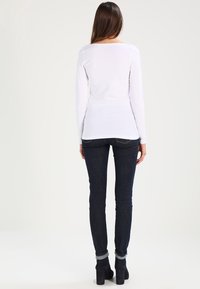 Weißes Langarmoberteil mit rundem Halsausschnitt kombiniert mit dunkelblauen Skinny-Jeans und schwarzen Stiefeletten mit umgeschlagenem Schaft.