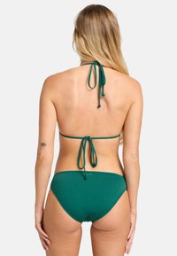 Zelený bikiny set s halter výstrihom a viazaním, doplnený o zodpovedajúce spodné diely. Hladká tkanina s minimalistickým dizajnom a nastaviteľnými prvkami.