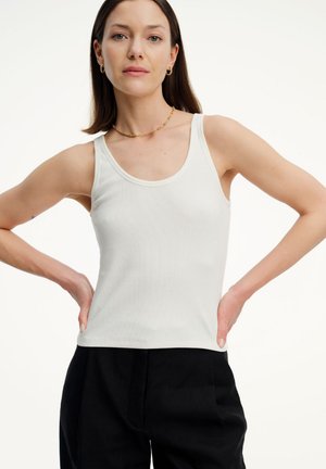 Biały prążkowany top na ramiączkach z okrągłym dekoltem i szerokimi ramiączkami, połączony z czarnymi spodniami. Minimalistyczny design, lekki materiał.