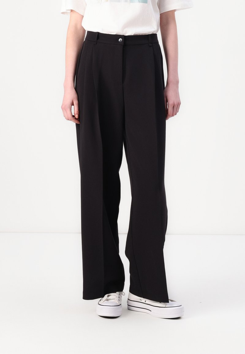 Black wide-leg trousers with a high waist, featuring a single button closure and belt loops. Smooth fabric, paired with white sneakers.