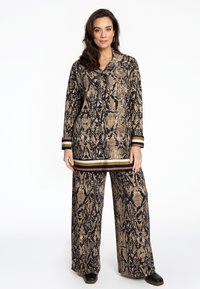 Outfit mit Schlangenhautmuster, bestehend aus einem Langarmoberteil mit Kragen und weit geschnittenen Hosen. Die Farben sind Schwarz, Gold und Beige, mit gestreiften Akzenten.