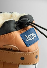 Narancssárga nylon csizma fekete felsőrésszel, fehér bolyhos béléssel, kék gumilogo folttal és barna, pöttyös részletezésű pánttal. Állítható húzózsinór zárás.
