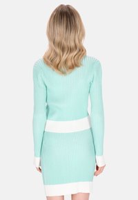 Rochie tricotată în nuanță verde mentă, cu dungi şi model cu şnur cu nervuri, mâneci lungi și accente albe la tiv și manșete. Design conic, lungime medie.