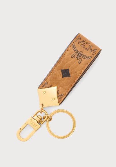Porte-clés en cuir avec sangle couleur camel ornée du logo et de symboles MCM noirs, relié à un anneau et un mousqueton dorés.