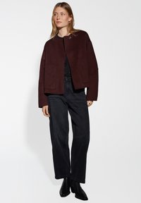 Bordeaux cropped jack met een ronde halslijn, voor sluiting met knopen en twee grote zakken, gecombineerd met zwarte wijde jeans en enkellaarsjes.