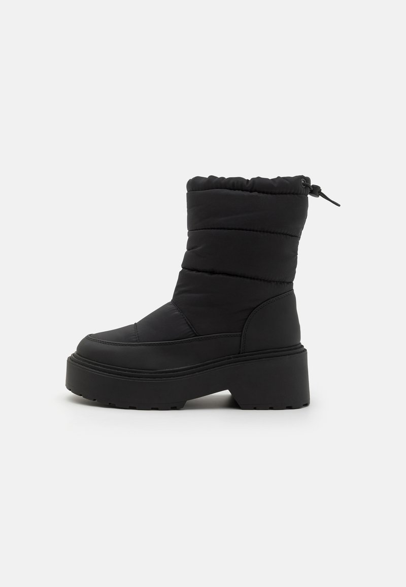 Bottines noires jusqu'à la cheville avec un dessus matelassé, une semelle compensée et un col élastiqué. Le matériau est lisse avec une finition mate et des accents texturés.