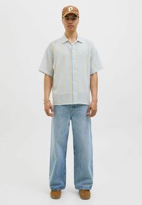 Korte mouwen lichtblauwe shirt met verticale strepen, gecombineerd met losse lichte denim jeans en bruine schoenen; heeft knoopsluiting en een ontspannen pasvorm.