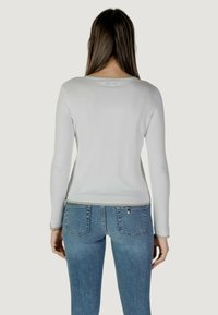 Maglietta bianca a maniche lunghe con scollatura rotonda e orlo a coste, abbinata a jeans blu aderenti con tasche posteriori e un accento con logo discreto.
