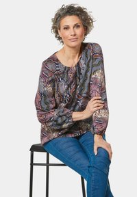 Langärmlige Bluse im bunten Schlangenprint mit lila, grün und beige Mustern. Weicher Stoff mit rundem Halsausschnitt und gerafften Ärmeln.