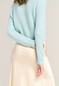 Light blue, knitted sweater with a soft, fuzzy texture, paired with a beige satin skirt. The sweater has a relaxed fit and long sleeves.