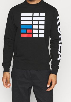 Schwarzer Sweatshirt mit weißen Blockmustern und einem blau-roten Akzent, mit "KOREA" in großen weißen Buchstaben auf dem Ärmel gedruckt.