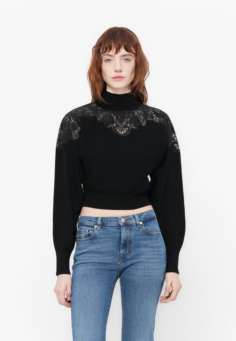 Maglione nero corto con maniche lunghe e colletto alto, dotato di un sopra in pizzo sulle spalle e texture a coste sull'orlo.