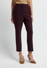 Pantalons taillés bordeaux avec des détails de pinces, longueur cheville, taille haute, associés à des chaussures à talons hauts couleur beige. Tissu lisse et structuré.