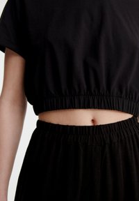 Černý zkrácený top s elastickým pasem, doplněný volnými černými kalhotami, které mají hladkou texturu a jednoduchý design.