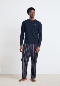 Marine langærmet skjorte med hvidt logo, parret med pyjamasbukser med stribemønster i mørke farver med røde, blå og grønne accenter.