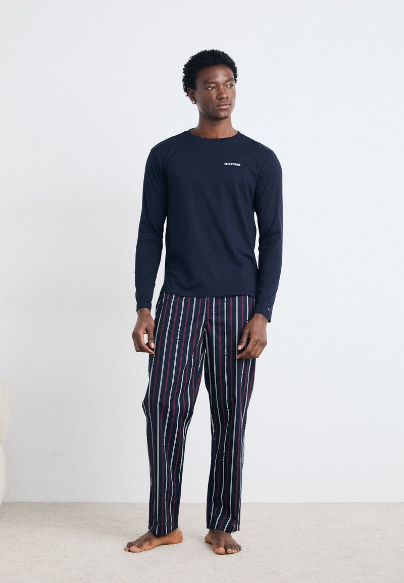 Marine langærmet skjorte med hvidt logo, parret med pyjamasbukser med stribemønster i mørke farver med røde, blå og grønne accenter.