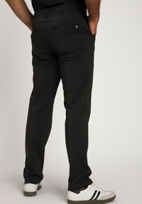 Pantaloni neri, leggeri e elasticizzati con una texture liscia, dotati di una tasca posteriore con zip e una vestibilità sartoriale. Indossati con scarpe da ginnastica bianche.