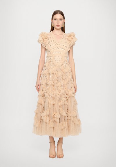 Robe longue en tulle nude avec un corsage froncé et des volants qui se déploient sur la jupe. Présente des accents scintillants et des manches courtes froncées.