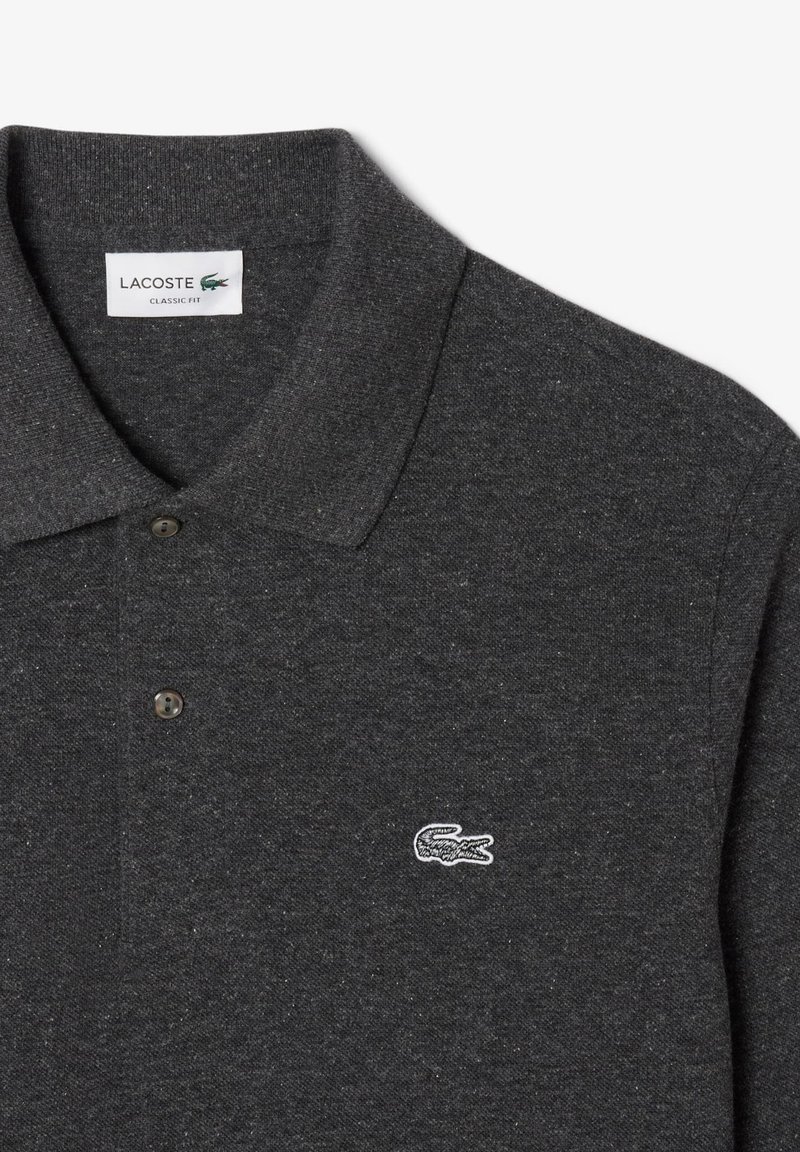 Polo shirt gris foncé avec une coupe classique, col court, deux boutons noirs et un petit logo de crocodile brodé blanc sur la poitrine.