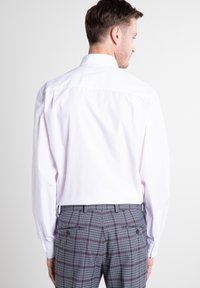 Witte longsleeve shirt met een button-down kraag, gecombineerd met grijze paneelbroek met donkere accenten en een getailleerde pasvorm.