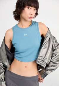 Light blue cropped tank top with ribbed texture and a small white Nike logo, paired with a shiny silver bomber jacket.