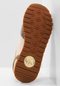 Podeszwa sneakersów z teksturowaną brązową gumą, z okrągłymi wzorami i złotym logo MK akcentującym bok w celu identyfikacji marki.