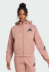 Sudadera con cremallera rosa con capucha, que presenta una tela texturizada, bolsillo delantero y acentos de logo negro en el pecho y las mangas.