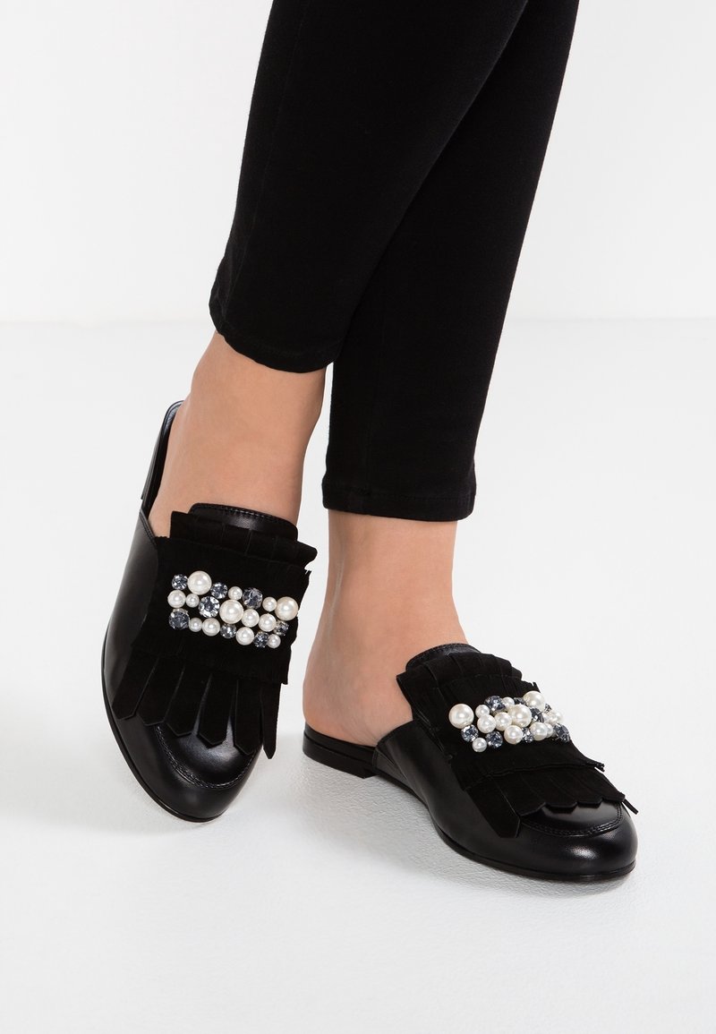 Svarta mule-skor i läder och mocka, med fransdetaljer och en dekorativ klunga av pärlor och rhinstenar på framsidan.