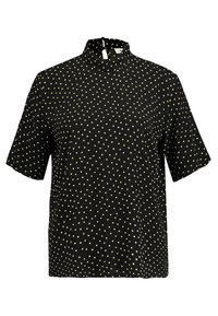 Kortärmad svart blus med hög hals, med ett gult prickmönster genom hela plagget och knäppning i nacken bak. Slät gardin.