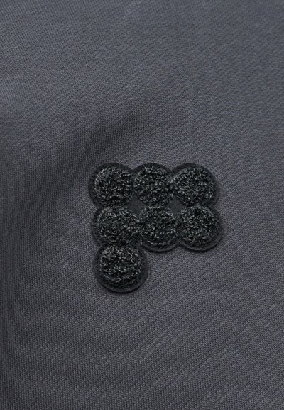 Tissu gris foncé avec un patch de sept points Velcro noirs texturés, étroitement regroupés en forme de L.