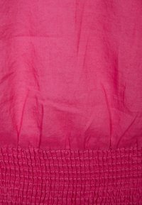 Fuchsia tyg med en slät textur och synliga rynkor, samt en samlad smockdetalj vid nederkanten.