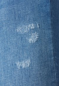 Lichtblauwe denimstof met een gestructureerde weving, met franjes op bepaalde plekken en lichte vervaging, wat wijst op een versleten ontwerp.