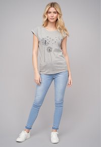 T-shirt gris à manches courtes avec un motif de pissenlit, associé à un jean skinny bleu clair et des baskets blanches. Tenue simple et décontractée.