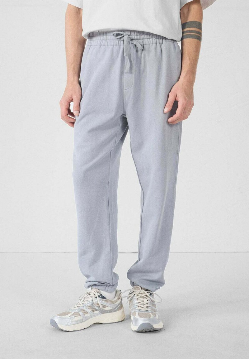 Lichtgrijze joggers met een elastische tailleband en koord. Stof heeft een gladde textuur, met zijzakken en taps toelopende boorden.