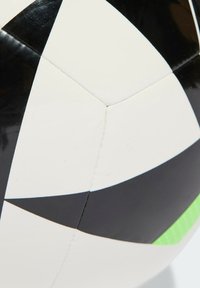 Černobílý fotbalový míč s geometrickým patchworkovým designem, hladkým povrchem a viditelnými švy. Doplňková zelená pruh.