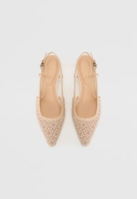 Paire de ballerines slingback beiges à bouts pointus avec un motif géométrique tissé sur fond blanc.