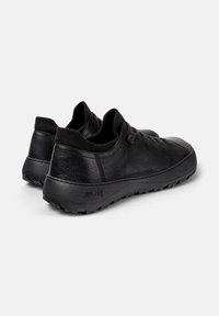 Zapatos de cuero negro con acabado texturizado, que presentan un corte bajo, suela de goma resistente, cuello elástico y marca en relieve en el talón.