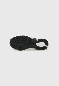 Chaussure de sport avec une semelle en caoutchouc noir présentant un motif de crampons, un dessus blanc avec des accents gris, et un talon renforcé. Texture lisse dans l'ensemble.