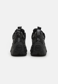Black athletic sneakers with textured rubber soles, padded collars, and pull tabs. The design features a bold logo printed on the sides.