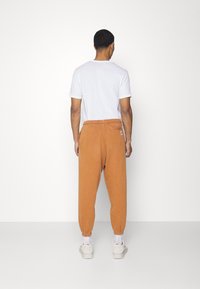 Men's orange sweatpants with elastic waistband and ankle cuffs, paired with a plain white t-shirt. Smooth texture, no visible patterns.